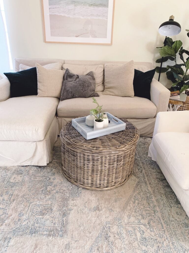 round gray washed woven coffee table styled with a blue striped tray and vases/planters.