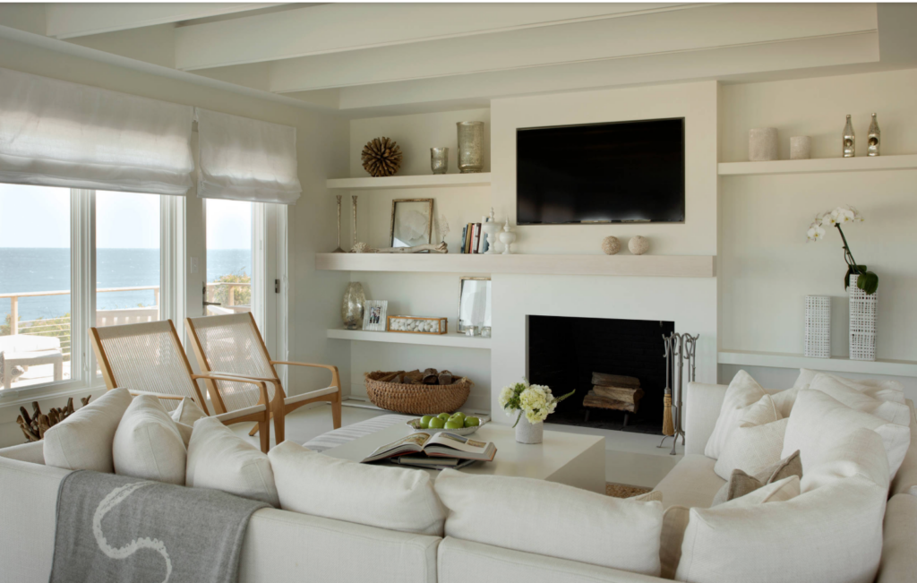 White living room floating shelves around a fireplace and a TV. The home overlooks the ocean and has large windows to enjoy the view.