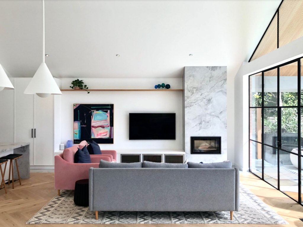 Living room with a high ceiling fireplace and floating shelves nearby.