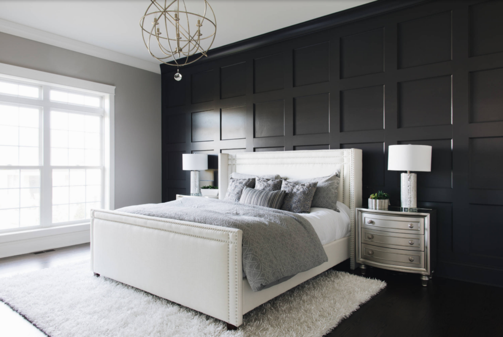 Black wood trim accent wall behind a bed in a master bedroom. The room has black wood flooring and light accent pieces.