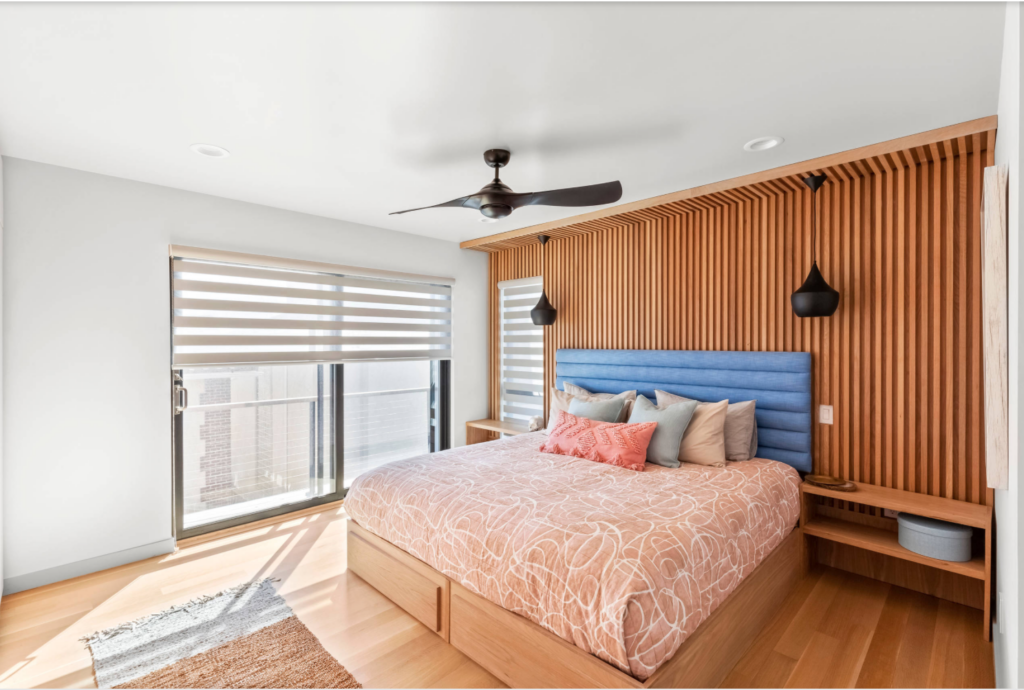 Fluted wood accent wall in a modern looking bedroom with a blue fabric headboard and light wood flooring.