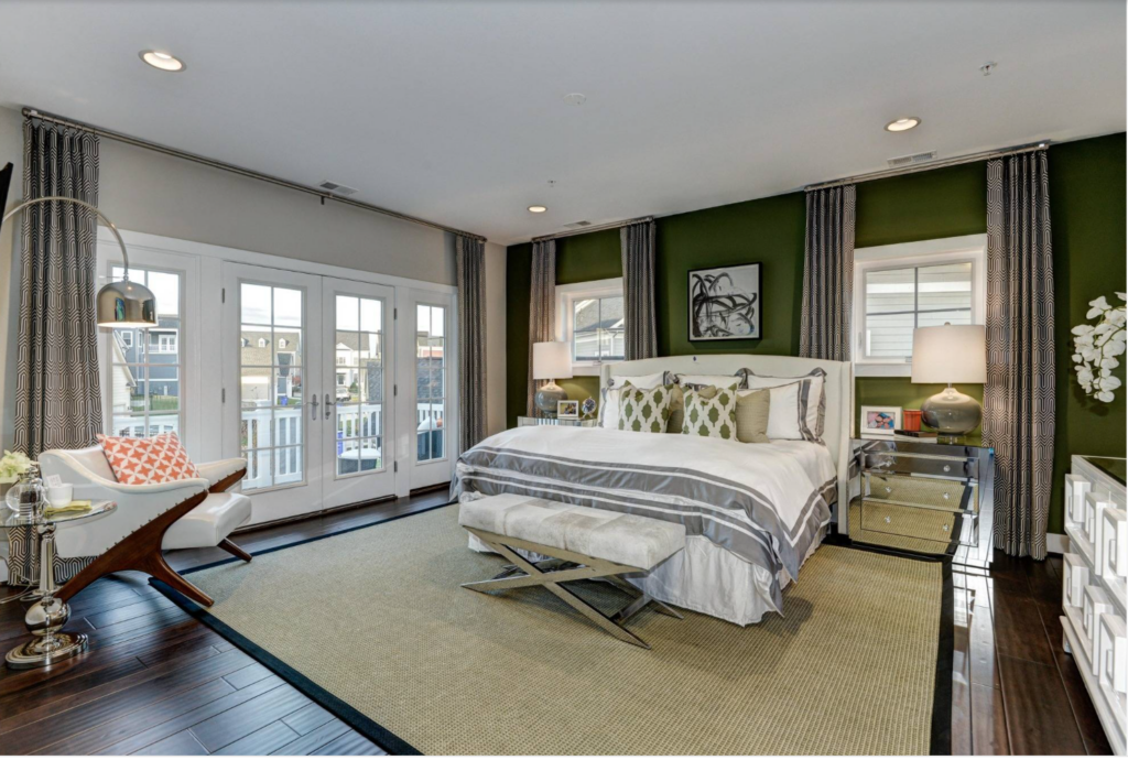 Green accent wall behind a bed in a large bedroom with wood floors and plenty of natural light.