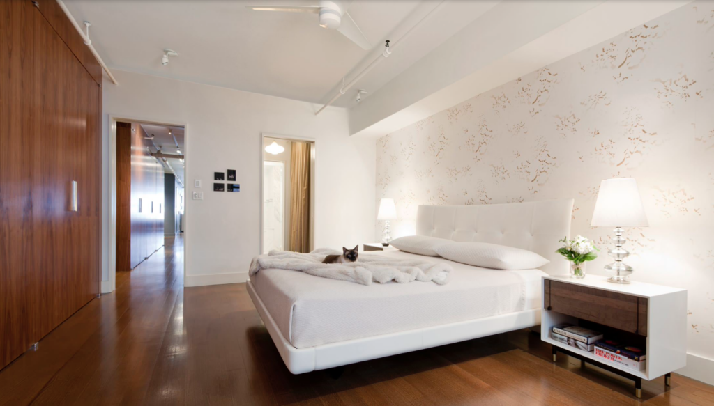 A bedroom with a high ceiling and a wallpaper accent wall.