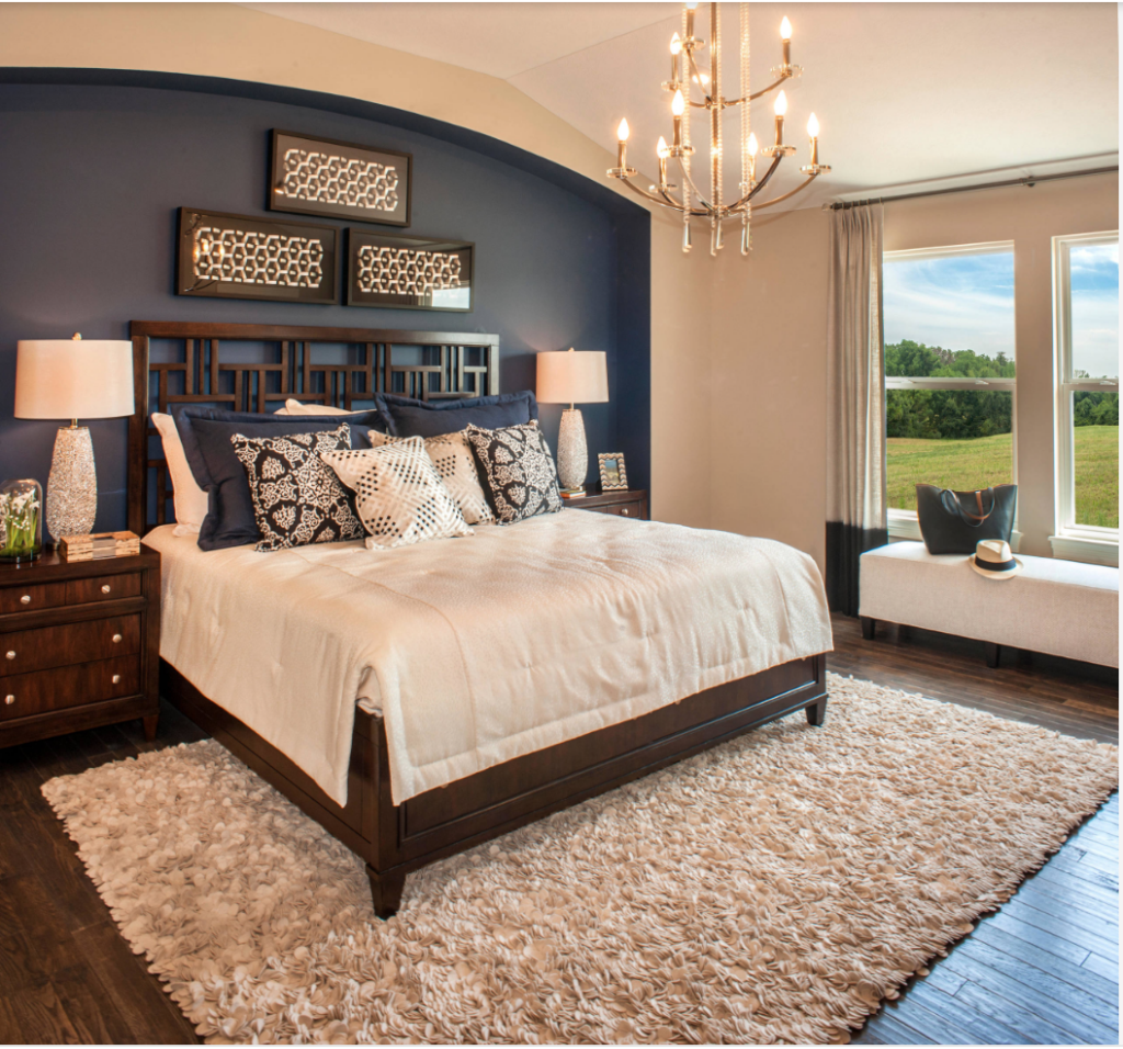 Navy blue accent wall behind a bed in a small bedroom with high ceilings and dark wood flooring.