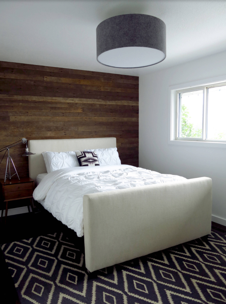 Rustic wood used to create a farmhouse inspired accent wall in a bedroom with a large light fixture and tons of natural lighting.