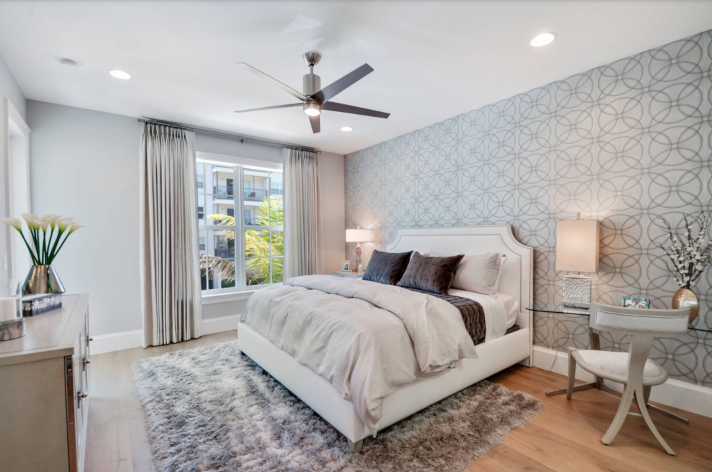 Wallpaper used as a behind the bed accent wall in a bedroom with light wood flooring and gray area rug.