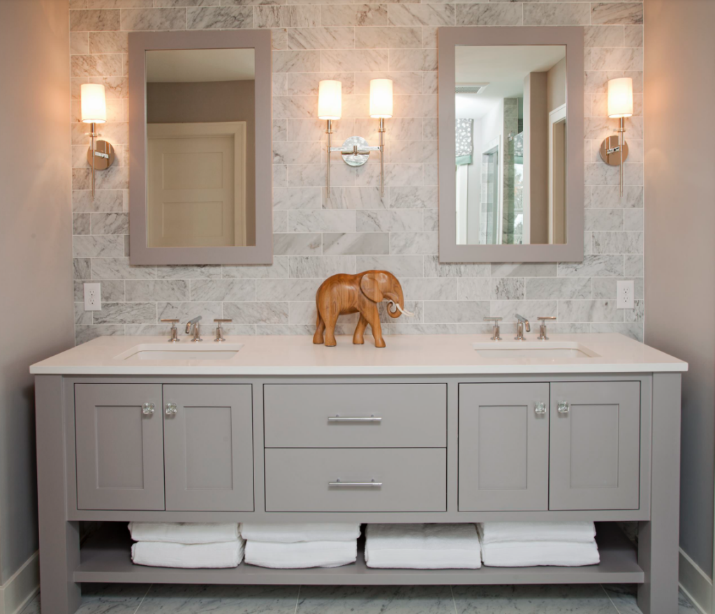 Light gray painted bathroom cabinte in a bright bathroom with marble tile backsplash.