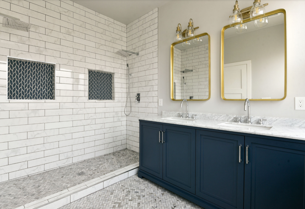 Navy blue bathrrom cabinets used in this bathroom that also has brass mirrors and brass light fixtures.