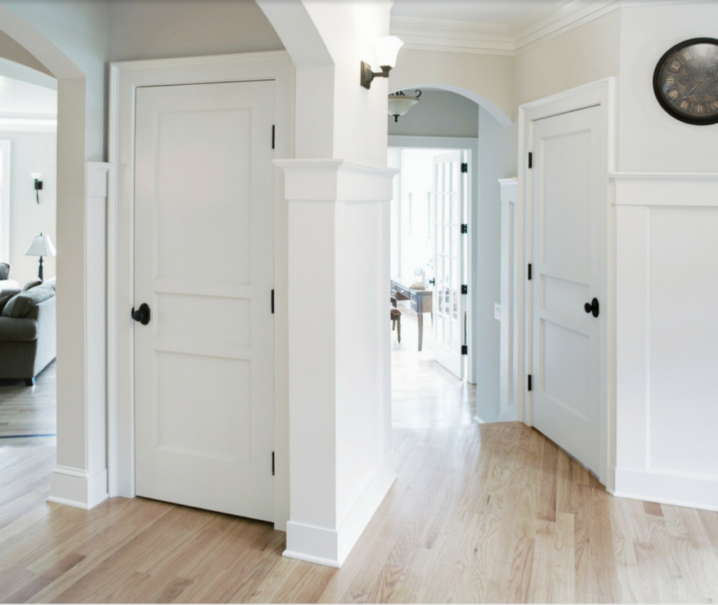 White painted interior doors with black hardware in a room with light wood flooring.
